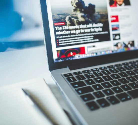 Open laptop displaying an online news article on a desk with a notebook nearby.